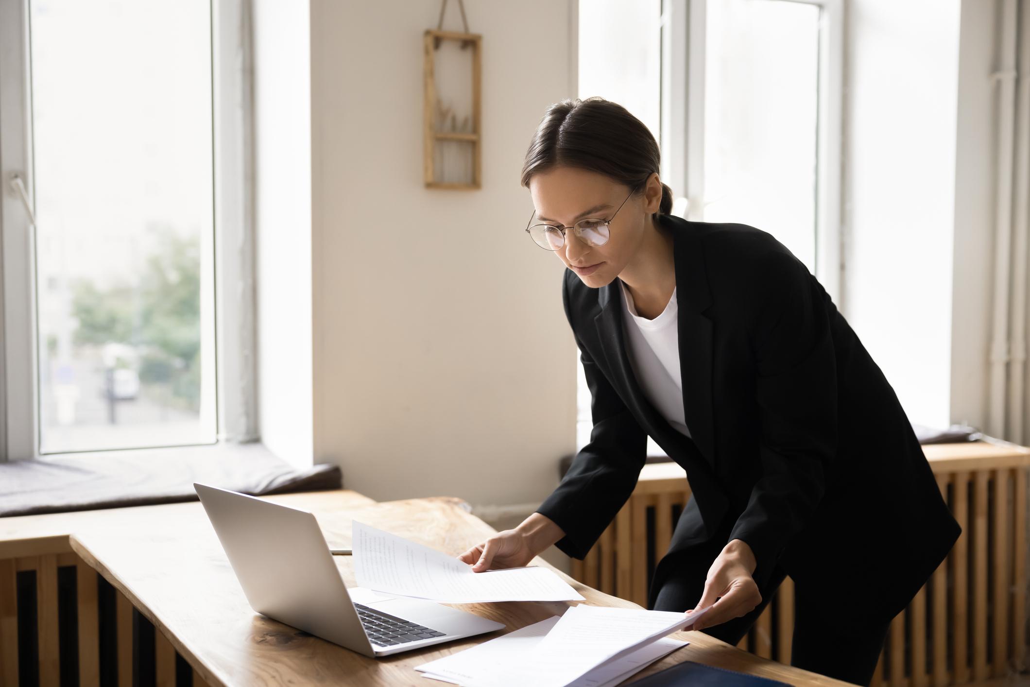 Profesional revisando documentos junto a una laptop en su escritorio